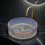 Transparent glass sink on a black marble countertop with a gold faucet.