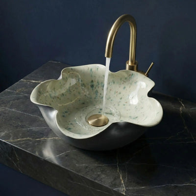 Decorative sink with a gold faucet on a dark marble surface against a blue background