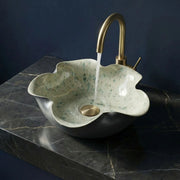 Decorative sink with a gold faucet on a dark marble surface against a blue background