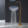 Glass sink with gold faucet against a dark wall