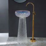Glass sink with gold faucet against a dark wall