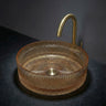 Round glass sink with gold faucet on a dark surface