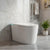 Modern freestanding bathtub in a bathroom with marble walls and a plant.