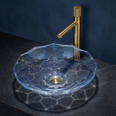 Clear glass sink with gold faucet against a dark background