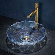 Clear glass sink with gold faucet against a dark background
