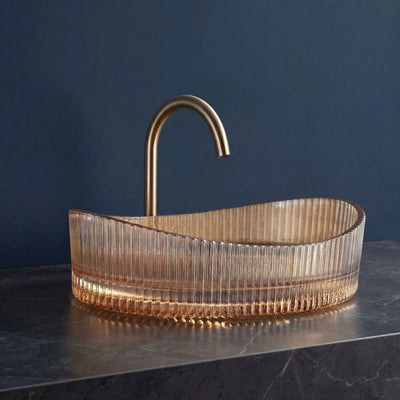 Modern glass sink with gold faucet against a dark blue wall
