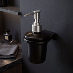 Black soap dispenser with silver pump on a dark wall in a bathroom setting.