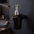 Black soap dispenser with silver pump on a dark wall in a bathroom setting.