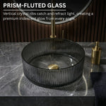 Prism-fluted glass sink on a dark marble countertop with gold fixtures.