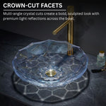 Glass sink with gold faucet on a dark surface, featuring crown-cut facets.